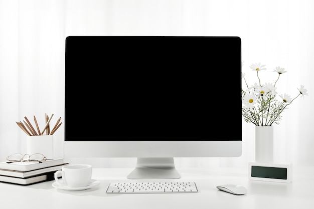 Primer plano de una computadora, una taza de café, un jarrón de flores y más en un escritorio blanco, en el interior