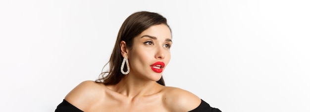 Primer plano de concepto de moda y belleza de mujer de lujo con aretes de labios rojos y vestido negro mirando aw