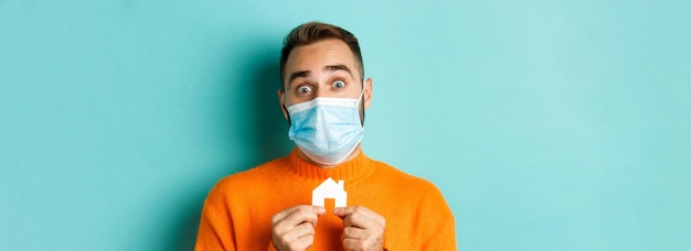 Primer plano del concepto de pandemia de bienes raíces y coronavirus de un hombre adulto con una máscara médica que sostiene un papel pequeño