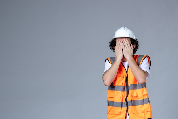 Foto gratuita primer plano del constructor masculino en chaleco de advertencia con casco de seguridad y cerrando su rostro sobre la pared gris de la ola