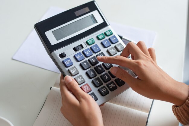 Primer plano de un contador usando una calculadora mientras examina un informe