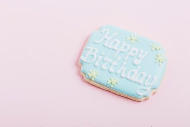 Primer plano de cookie con texto de feliz cumpleaños sobre fondo rosa