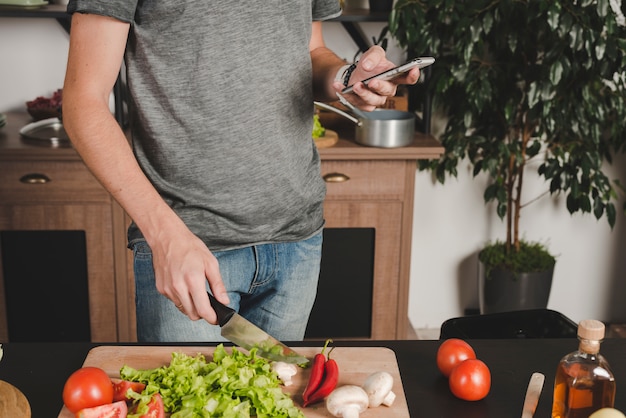 Primer plano de corte de verduras con cuchillo con teléfono móvil