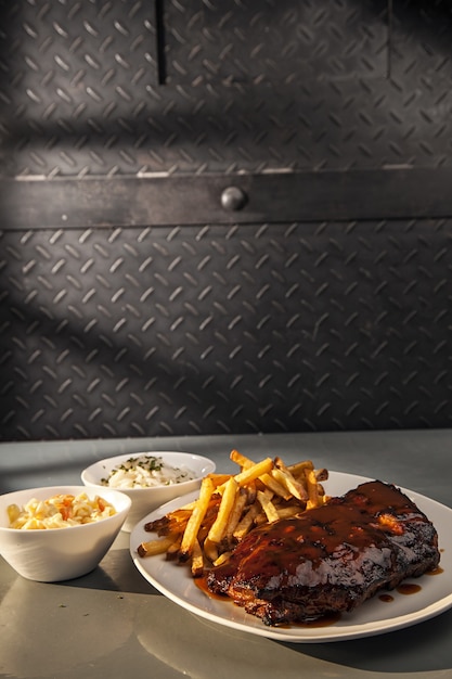 Foto gratuita primer plano de costillas de cerdo a la parrilla y papas fritas con ensalada en la mesa