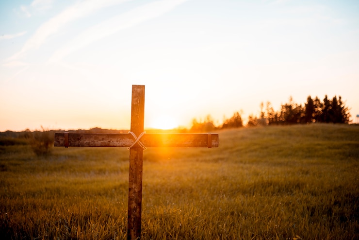 Foto gratuito un primer plano de una cruz de madera artesanal en el campo con el sol brillando
