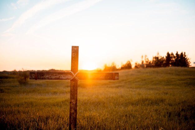 Un primer plano de una cruz de madera artesanal en el campo con el sol brillando