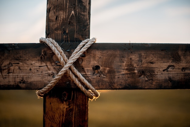 Primer plano de una cruz de madera con una cuerda envuelta y un fondo borroso