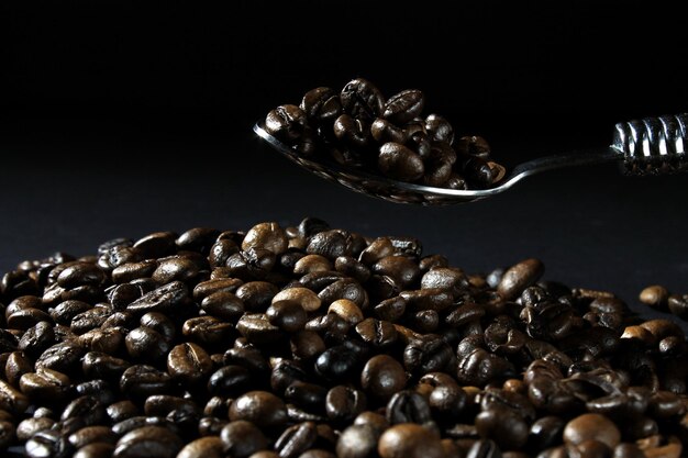 Primer plano de una cuchara que sostiene granos de café recién tostados contra un fondo oscuro