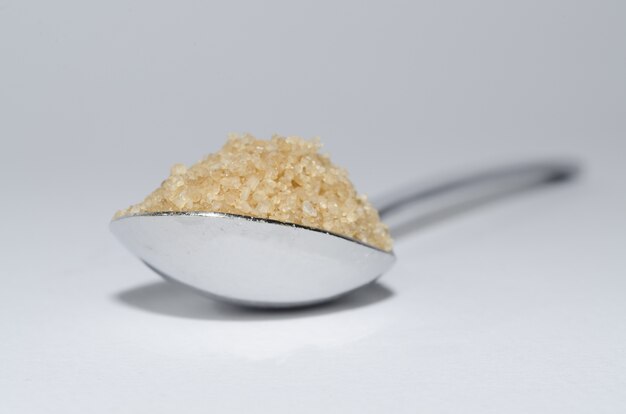 Primer plano de una cucharada de azúcar morena sobre la superficie blanca