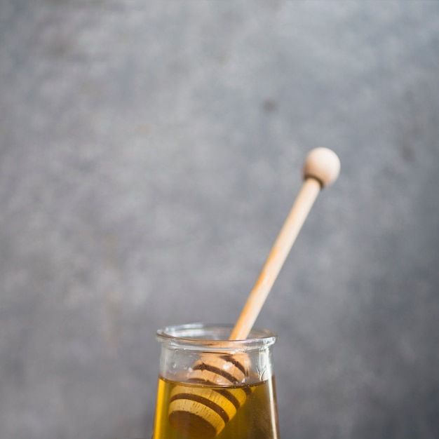 Primer plano de cucharón de miel en la olla de miel sobre el fondo gris