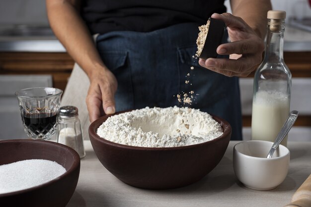 Primer plano de un cuenco lleno de harina con una persona vertiendo un ingrediente en él