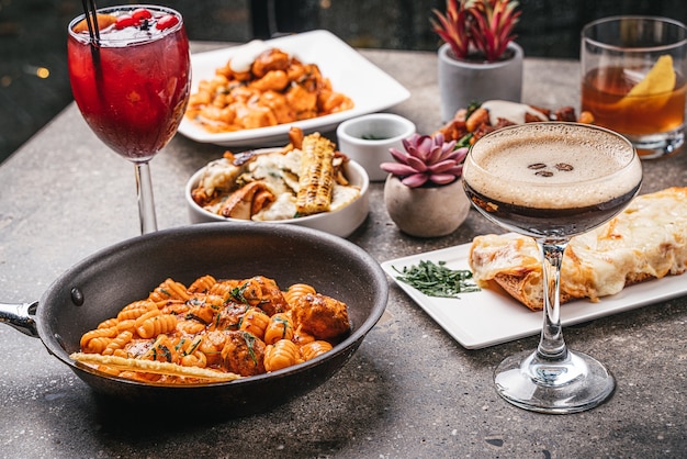 Primer plano de cuencos de pasta cocida con ensaladas, deliciosos cócteles y verduras fritas en la mesa