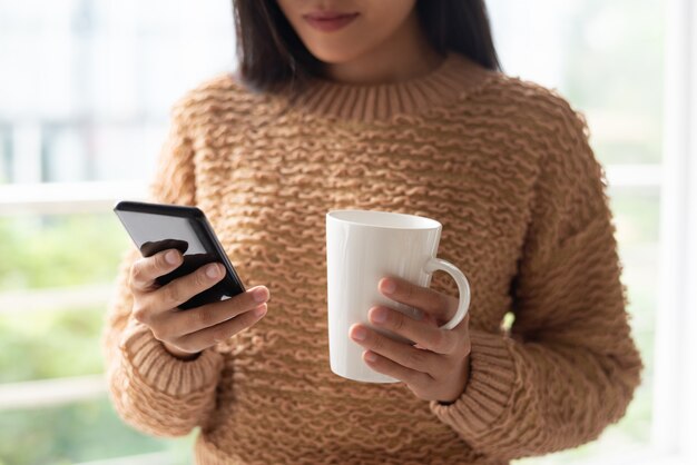 Primer plano de una dama seria usando un teléfono inteligente y tomando café