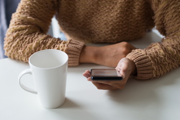 Primer plano de dama en suéter caliente con teléfono inteligente en la oficina