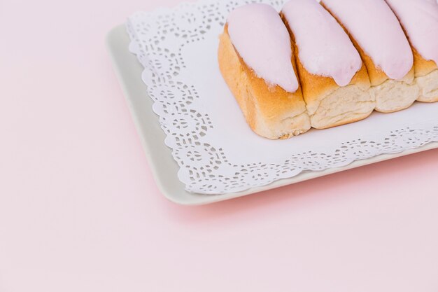 Primer plano de los dedos helados cubiertos con glaseado sobre la bandeja contra el fondo rosado