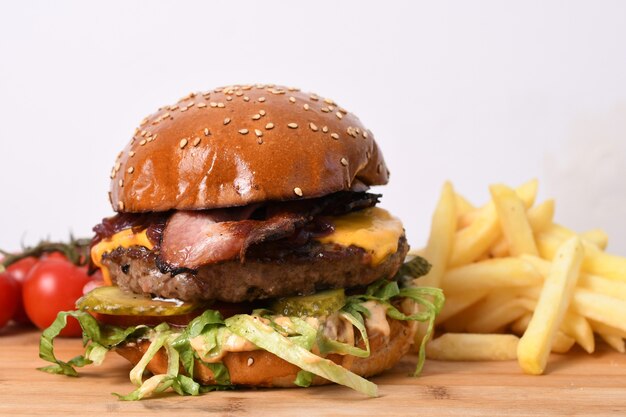 Primer plano de una deliciosa hamburguesa de ternera sobre una tabla de madera con papas fritas y tomates