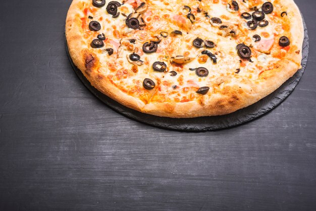 Primer plano de la deliciosa pizza en la pizarra sobre el fondo oscuro