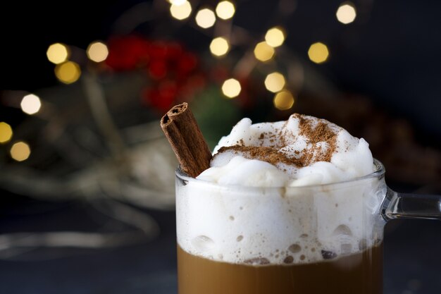 Primer plano de un delicioso café navideño con canela y espuma, frente a luces bokeh