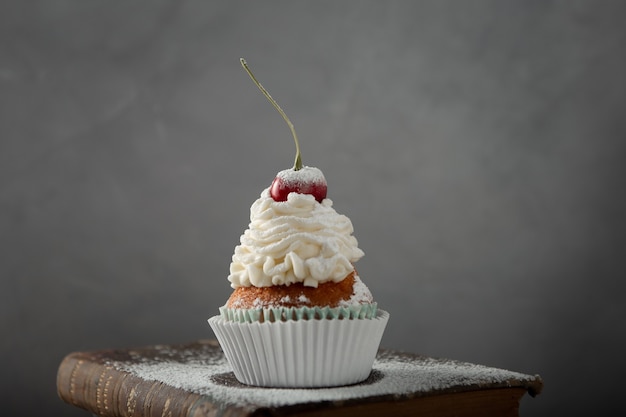 Primer plano de un delicioso cupcake con crema, azúcar en polvo y una cereza en la parte superior de un libro