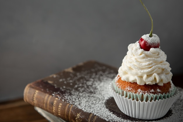 Primer plano de un delicioso cupcake con crema, azúcar en polvo y una cereza en la parte superior del libro