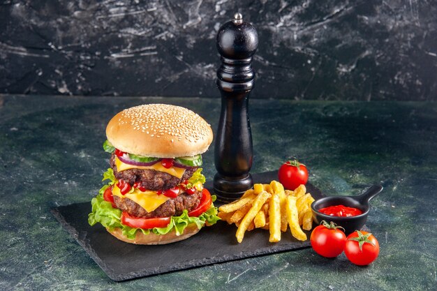 Primer plano de delicioso sándwich y papas fritas pimiento en tomates de bandeja de color oscuro sobre superficie negra