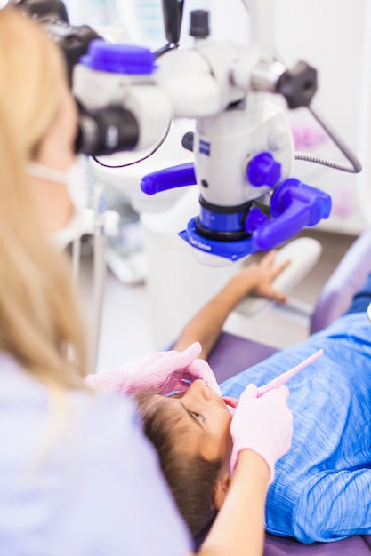 Primer plano de un dentista examinando los dientes de un niño con microscopio