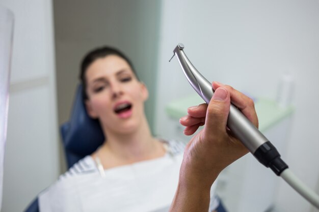 Primer plano del dentista sosteniendo una odontología, pieza de mano dental mientras examina a una mujer