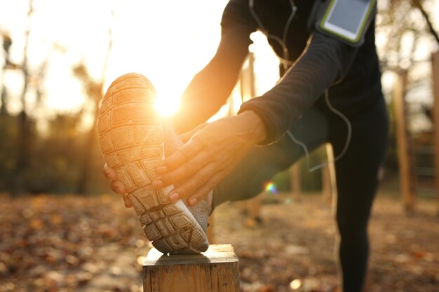 El primer plano de una deportista negra estirando su pierna mientras hace ejercicio en la naturaleza al atardecer