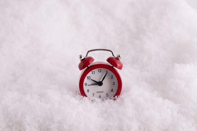 Primer plano de un despertador rojo en la nieve, un reloj contando el tiempo hasta el año nuevo