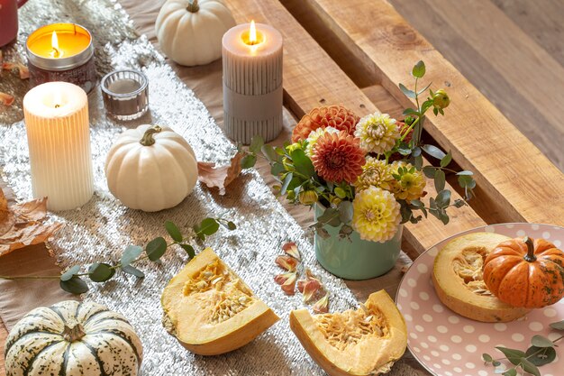 Primer plano de detalles de decoración acogedora de una mesa de comedor de otoño festivo con calabazas, flores y velas.