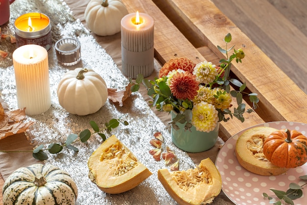 Primer plano de detalles de decoración acogedora de una mesa de comedor de otoño festivo con calabazas, flores y velas.