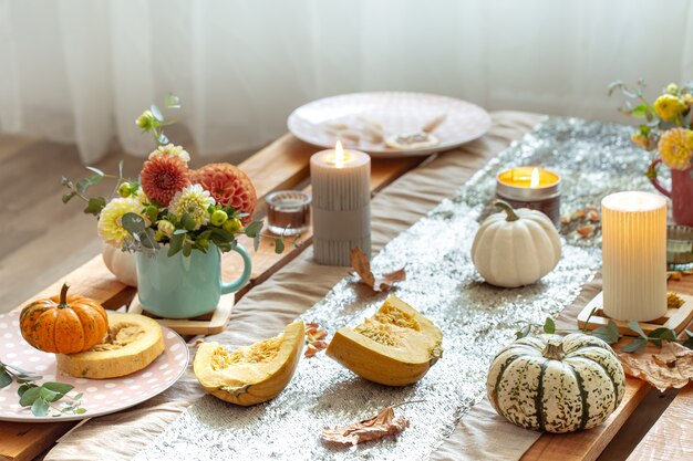 Primer plano de detalles de decoración acogedora de una mesa de comedor de otoño festivo con calabazas, flores y velas.