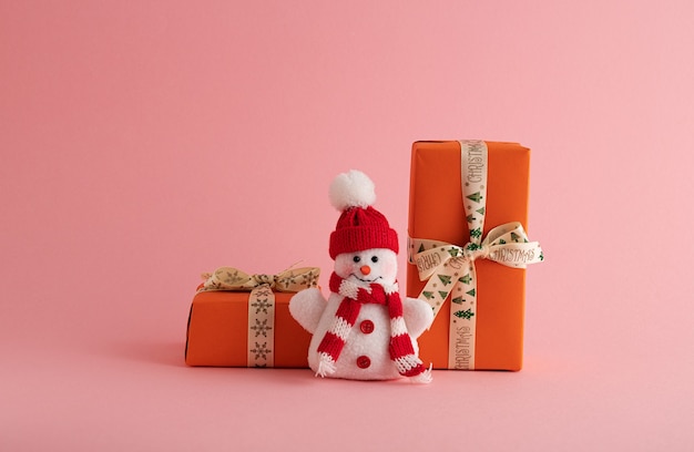 Primer plano de un divertido muñeco de nieve y cajas de regalo de color naranja en el fondo de color rosa