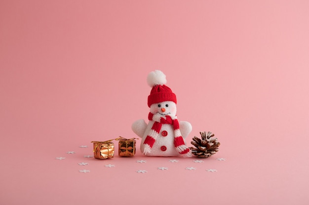 Primer plano de un divertido muñeco de nieve, pequeñas cajas de regalo y una piña en el fondo de color rosa