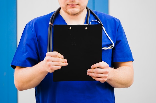 Primer plano de un doctor hombre sosteniendo portapapeles en la mano con estetoscopio alrededor de su cuello