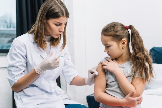 Primer plano de la doctora con guantes blancos en la mano dando la jeringa en el brazo del paciente