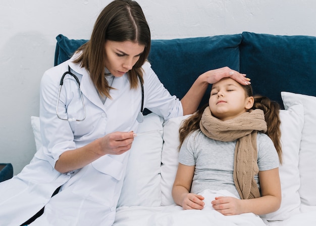 Primer plano de una doctora sentada cerca de la niña paciente mirando el termómetro