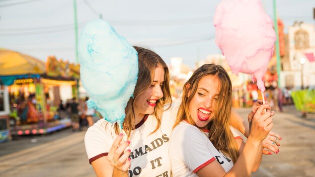 Primer plano de dos amigas felices con hilo de caramelo en el parque de atracciones