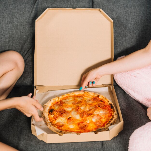 Primer plano de dos amigas tomando porciones de pizza de la caja
