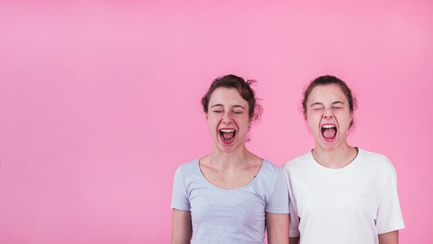 Primer plano de dos hermanas gritando contra el fondo rosa