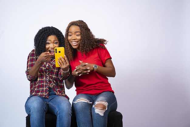 Primer plano de dos hermosas mujeres negras que parecen emocionadas mientras ven contenido juntos en un teléfono