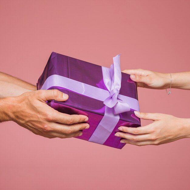 Primer plano de dos manos sosteniendo cajas de regalo púrpura sobre fondo de color