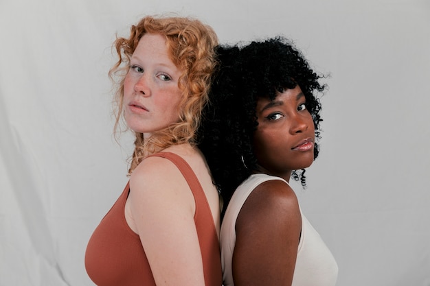 Foto gratuita primer plano de dos mujeres jóvenes multiétnicas de pie de espaldas contra el fondo gris