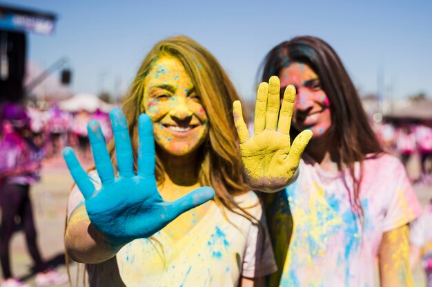 Primer plano de dos mujeres jóvenes que muestran sus manos pintadas con color holi