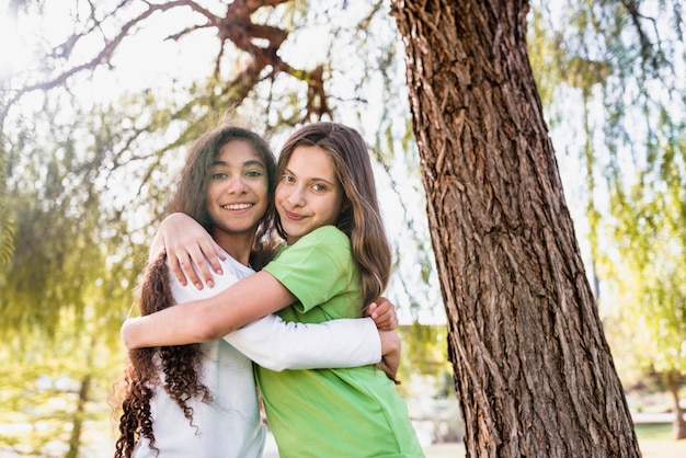 Primer plano de dos niñas de pie bajo el árbol abrazándose