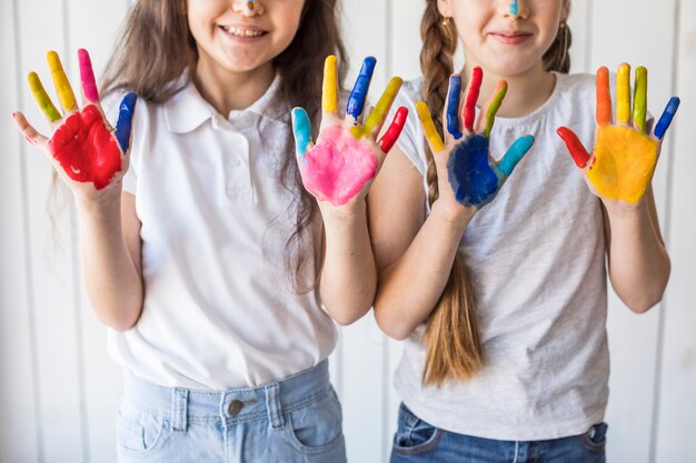 Primer plano de dos niñas sonrientes mostrando sus manos pintadas con color