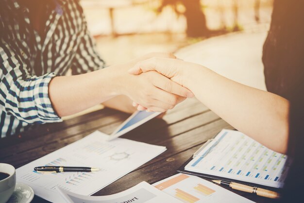 Primer plano de dos personas de negocios dándose la mano mientras está sentado en el lugar de trabajo.