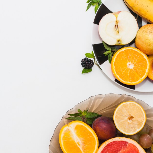 Primer plano de dos platos con frutas frescas a la mitad sobre fondo blanco