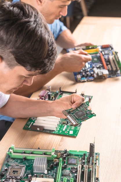 Primer plano de dos técnicos informáticos masculinos insertando el circuito en la placa madre de la computadora