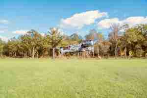 Foto gratuita primer plano de un dron volando sobre un campo verde junto a un bosque